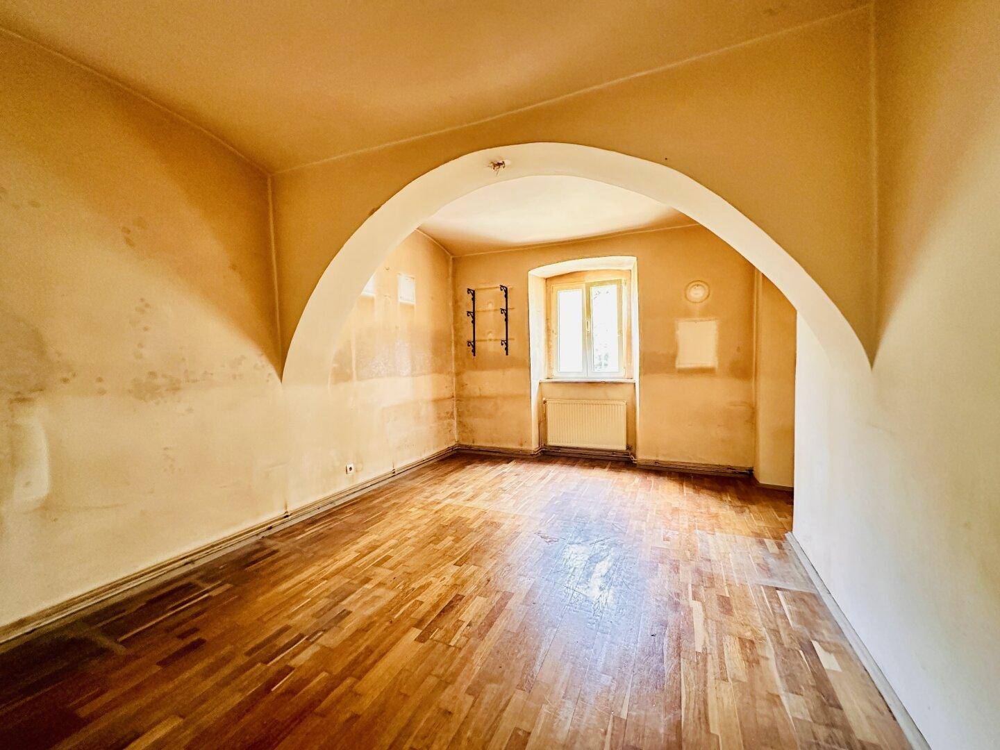 Heller Raum mit Holzboden, Gewölbedecken und Fenster, ideal für eine Renovierung.
