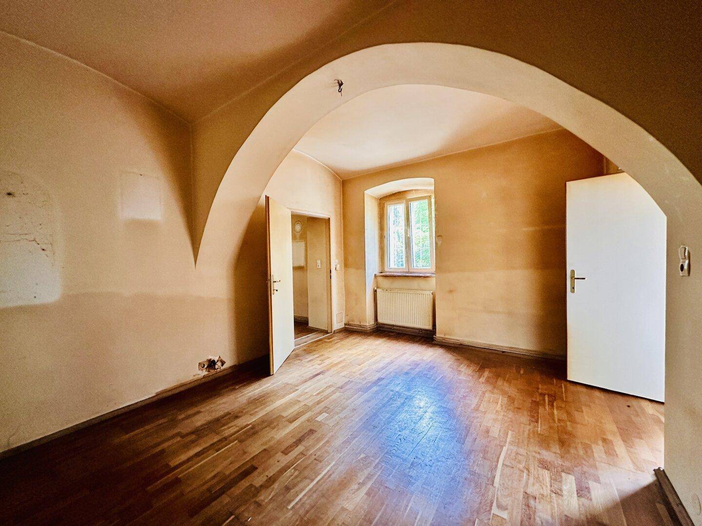 Großer Raum mit Holzboden, Gewölbedecken und Zugang zu weiteren Zimmern, renovierungsbedürftig.
