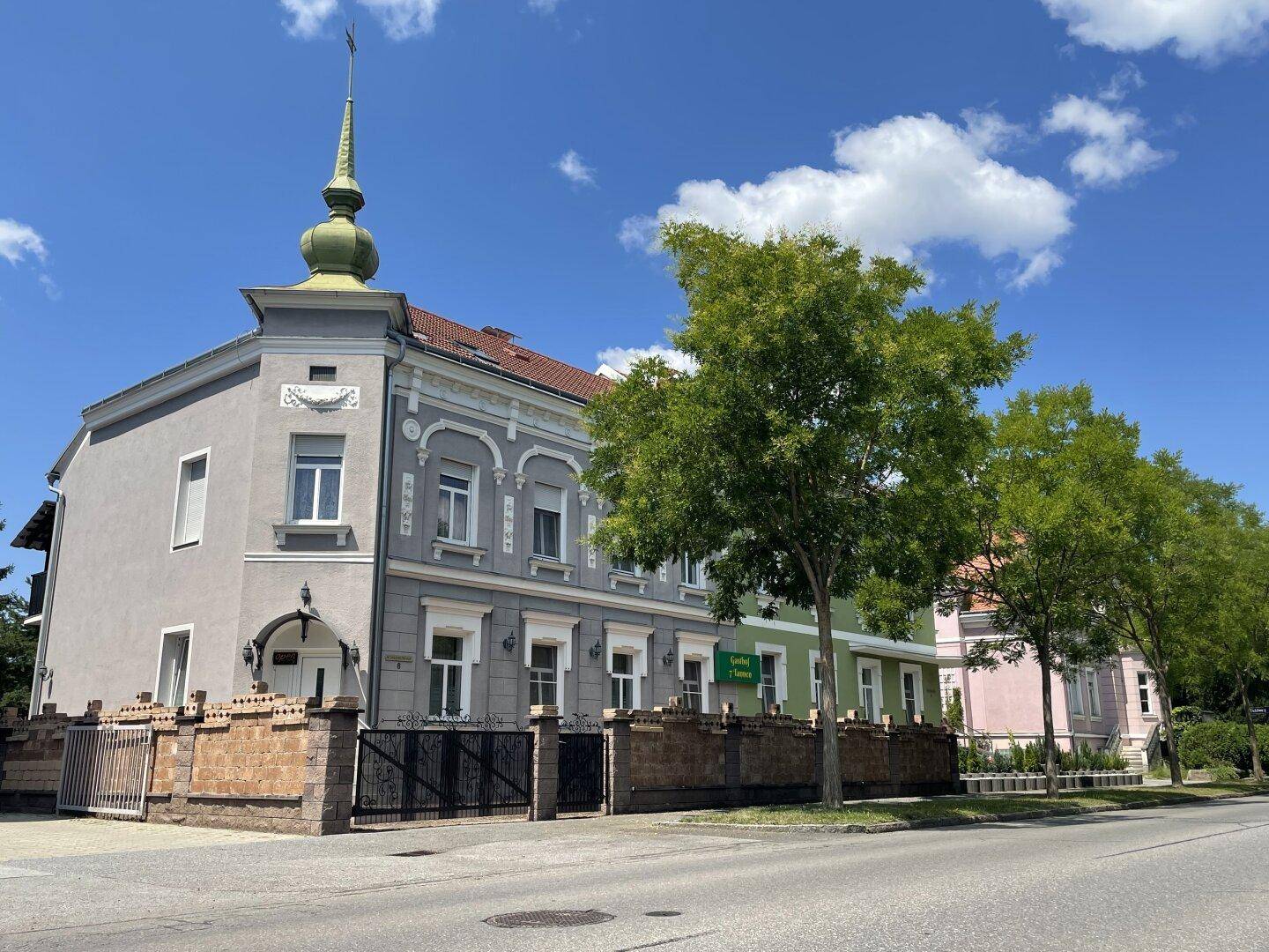 Historisches Gebäude mit markantem Turm und dekorativer Fassade an einer sonnigen Straße.