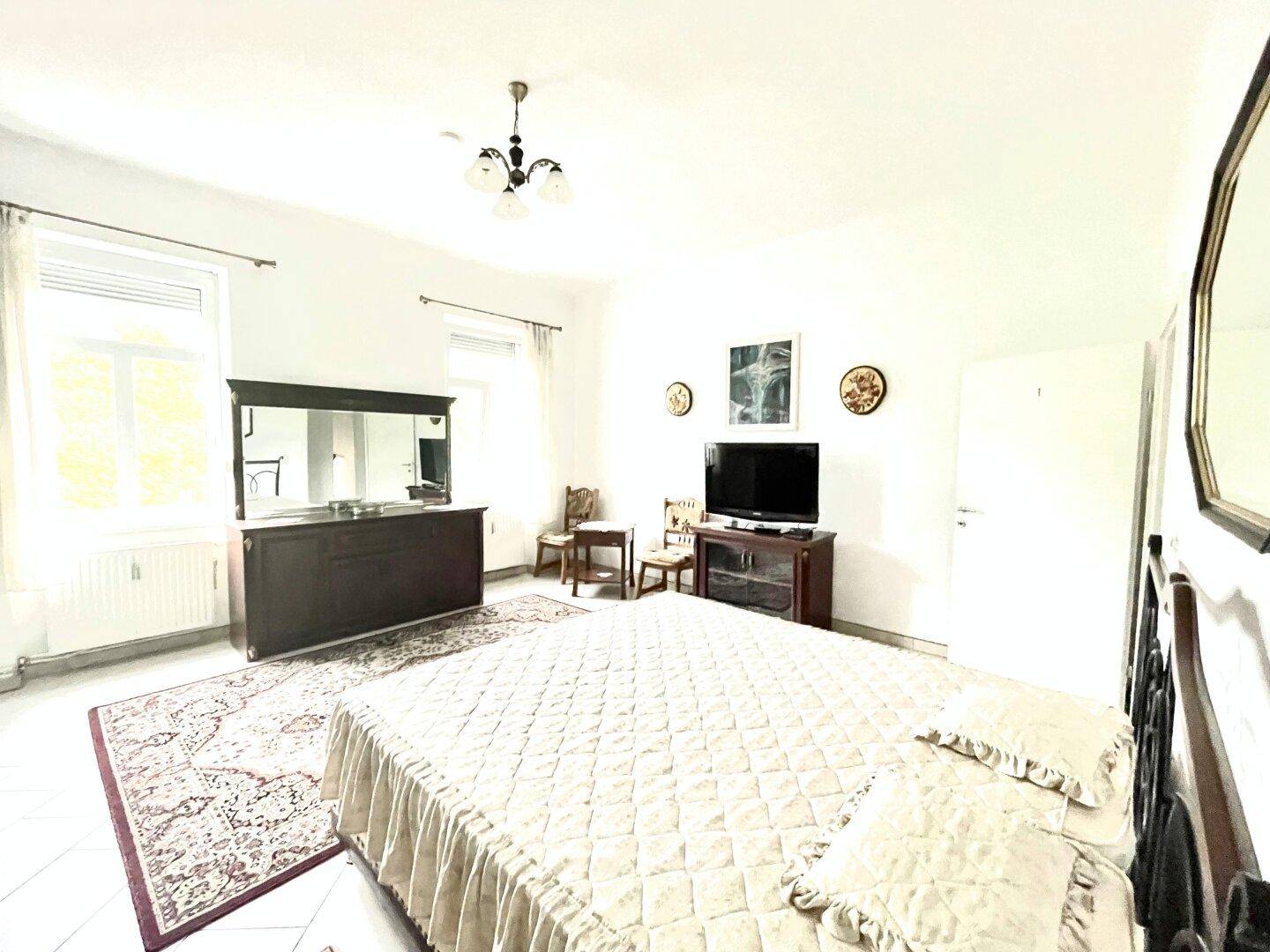 Helles Schlafzimmer mit Fliesenboden, einem großen Bett und dunklen Holzmöbeln.