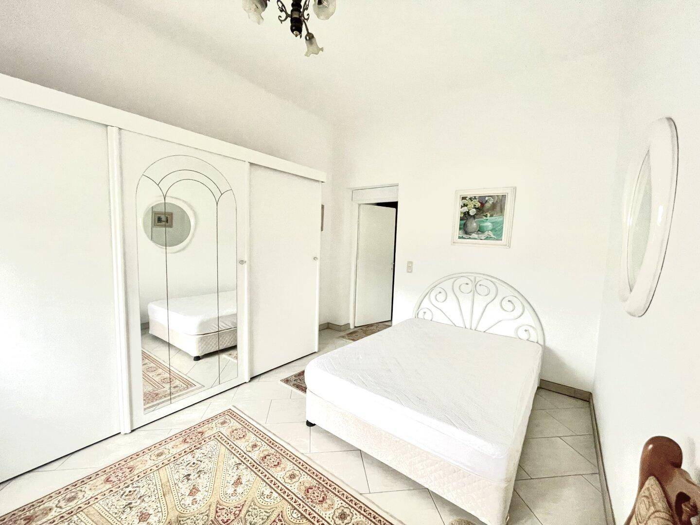 Helles Schlafzimmer mit weißem Schiebetürenschrank, Fliesenboden und einem Einzelbett.
