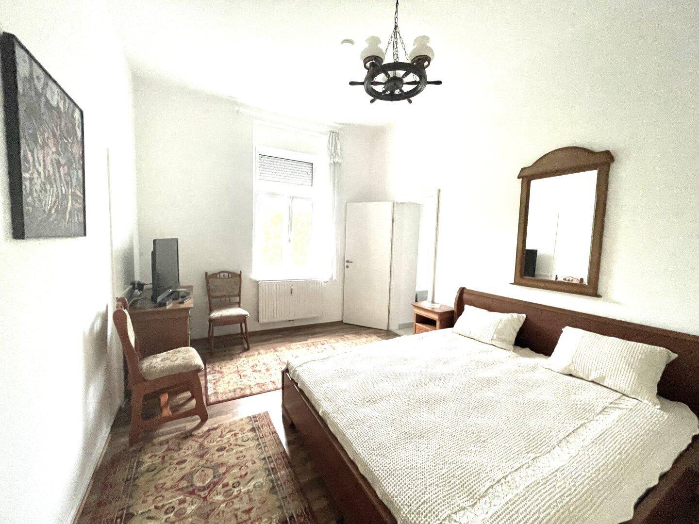Schlafzimmer mit Holzbett, Teppichboden, traditionellen Möbeln und einem Fenster.