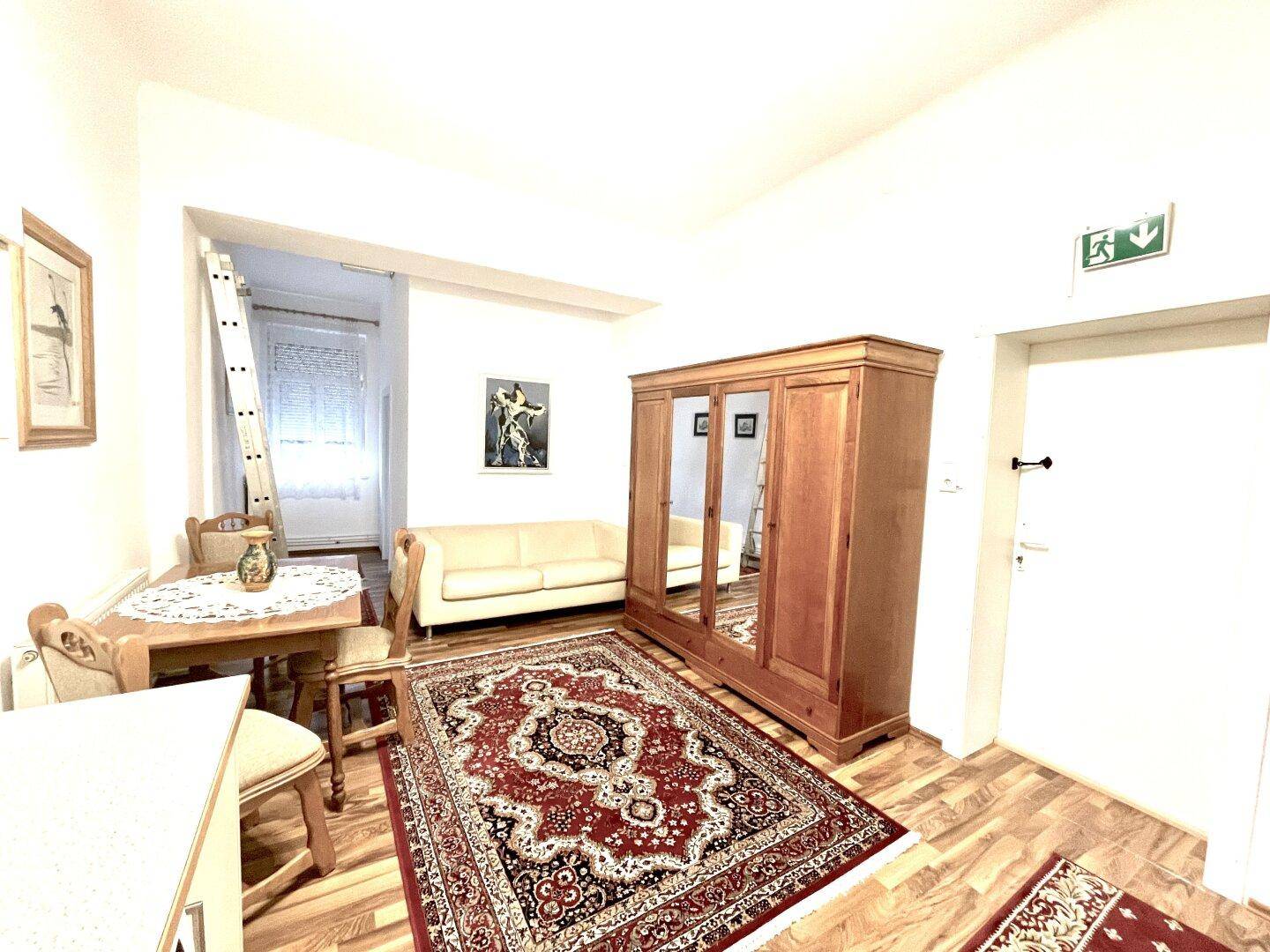 Wohnbereich mit Esstisch, Sofa und einem großen Holzschrank, verbunden mit einem weiteren Raum.