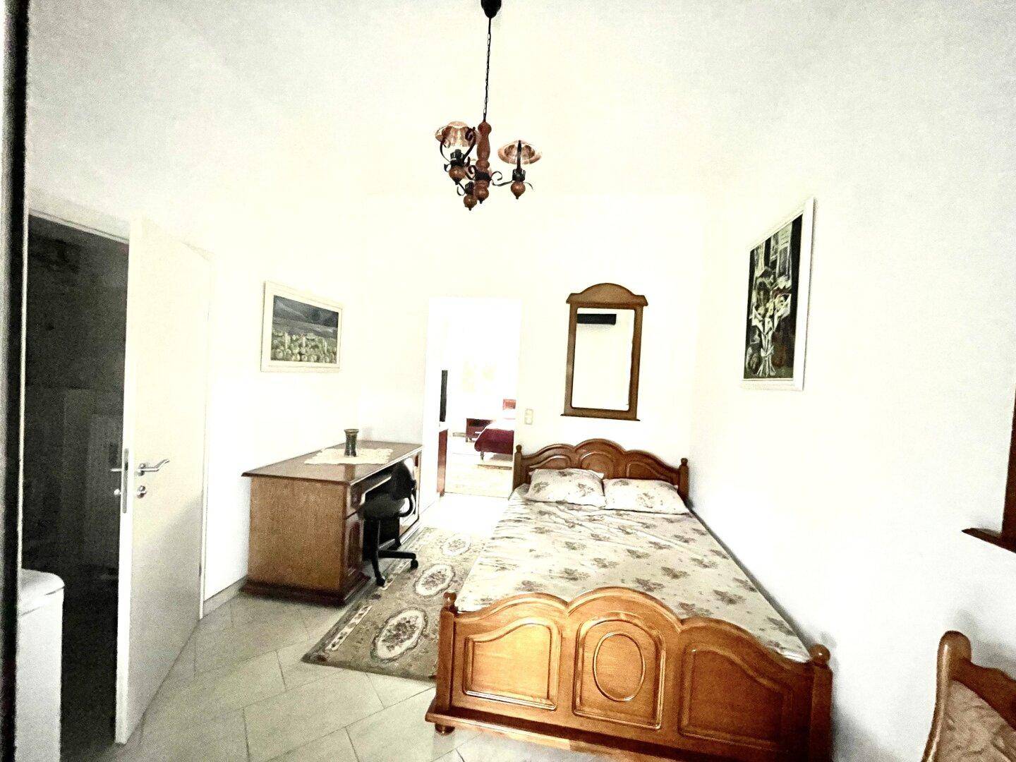Schlafzimmer mit Holzbett, Schreibtisch und Fliesenboden, hell und funktional eingerichtet.