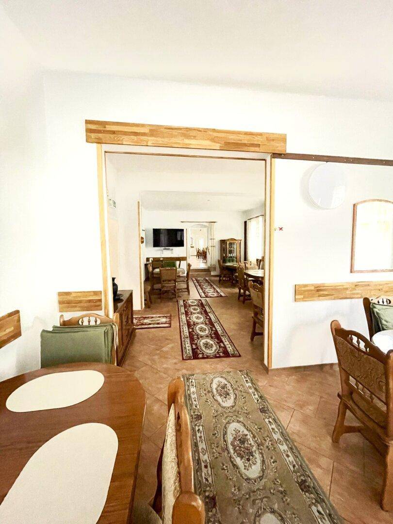 Geräumiger Essbereich mit mehreren Holztischen und traditionellen Teppichen, der zu weiteren Räumen führt.