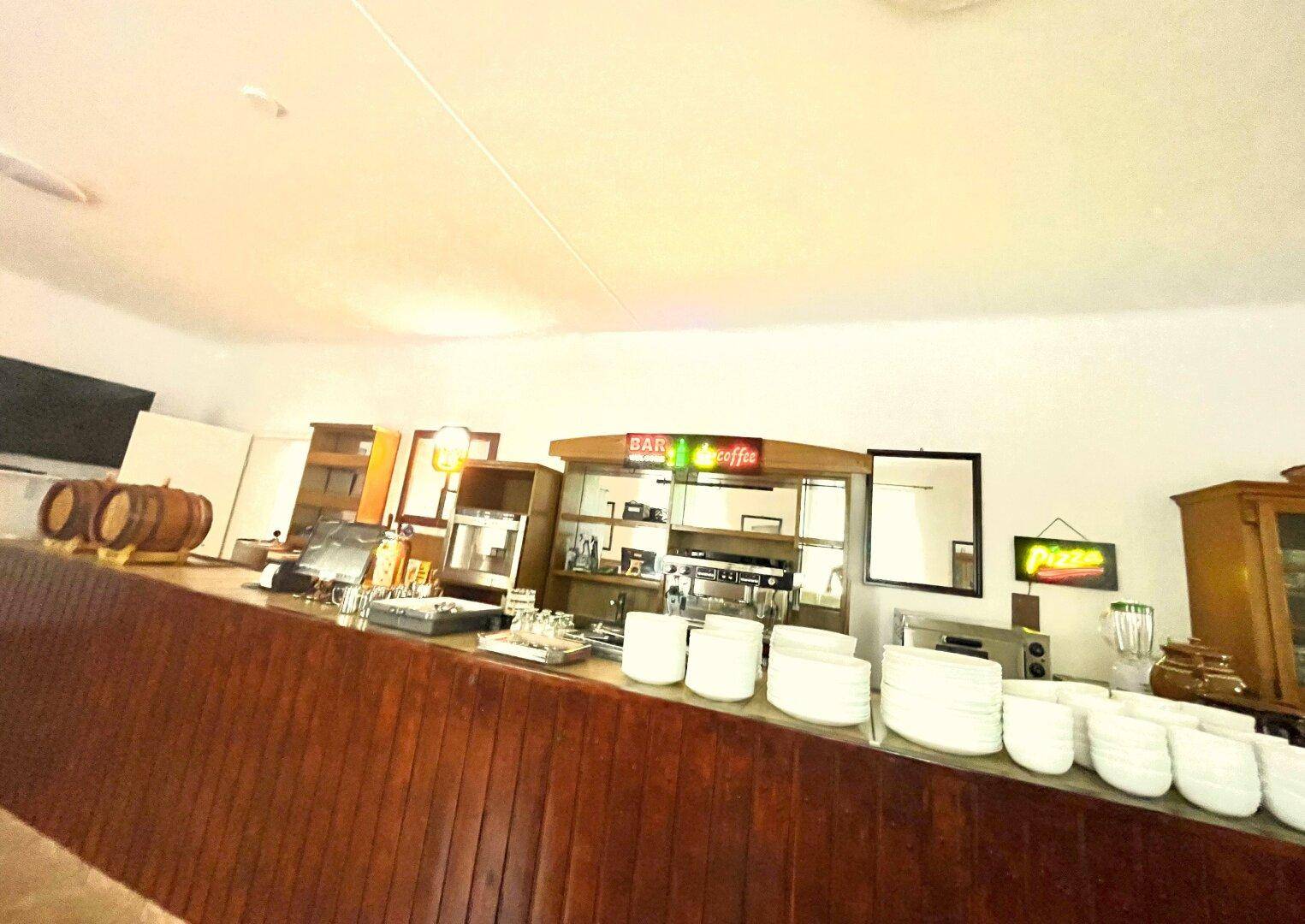 Detailansicht des Barbereichs mit Kaffeemaschine, Geschirr und traditionellen Holzfässern.
