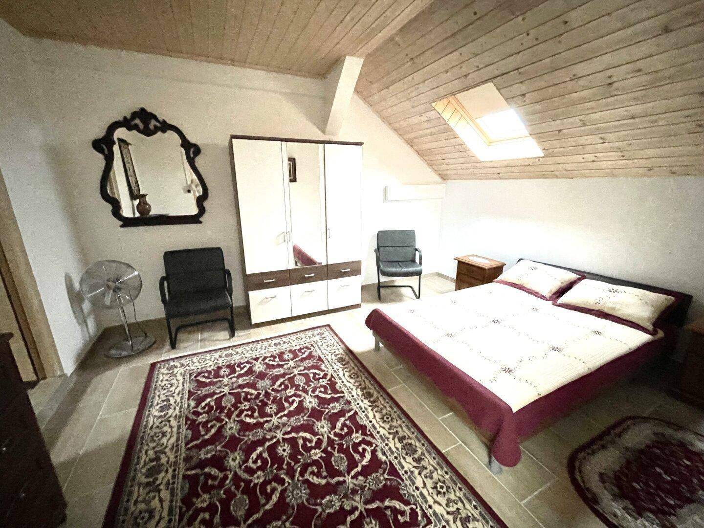 Gemütliches Schlafzimmer im Dachgeschoss mit Holzdachschrägen, Doppelbett und Dachfenster.