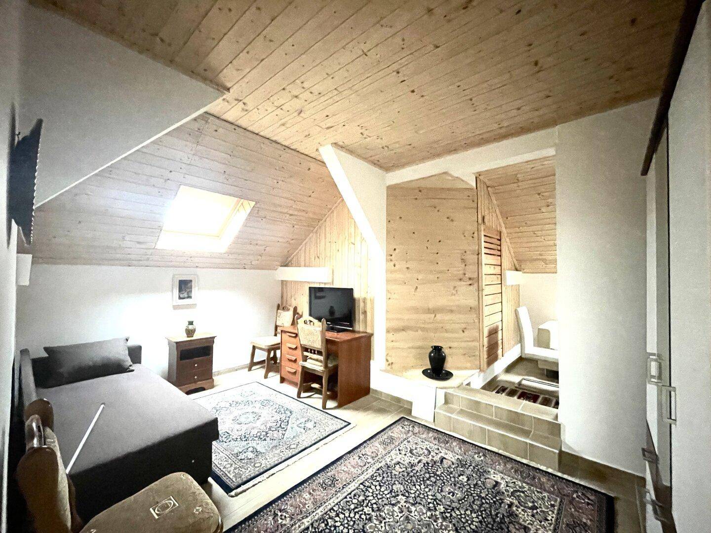 Dachgeschoss-Schlafzimmer mit Holztäfelung, Einzelbett, Schreibtisch und einem hellen Dachfenster.