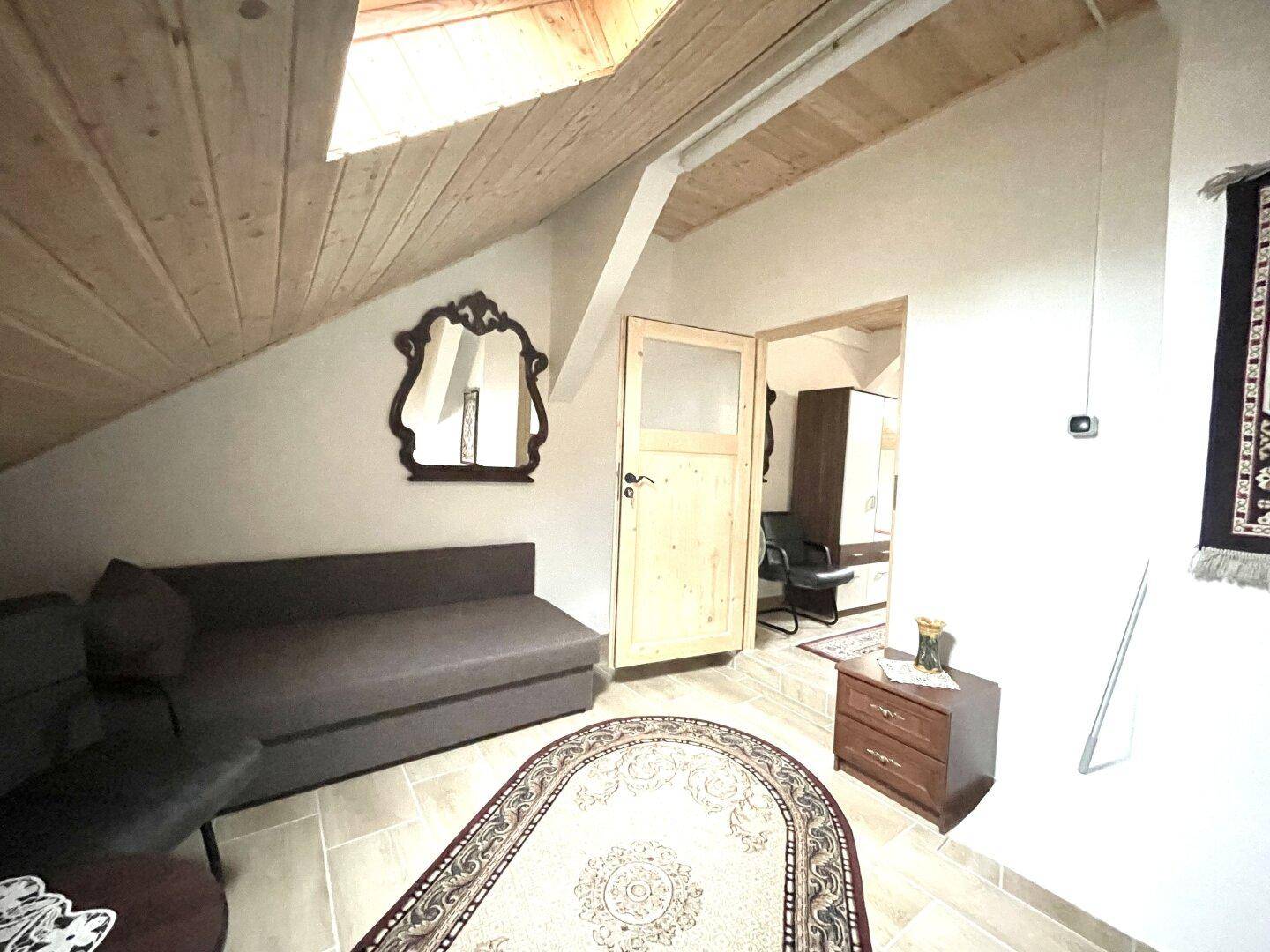Helles Schlafzimmer im Dachgeschoss mit Holzdachschrägen, Sofa und einem dekorativen Spiegel.