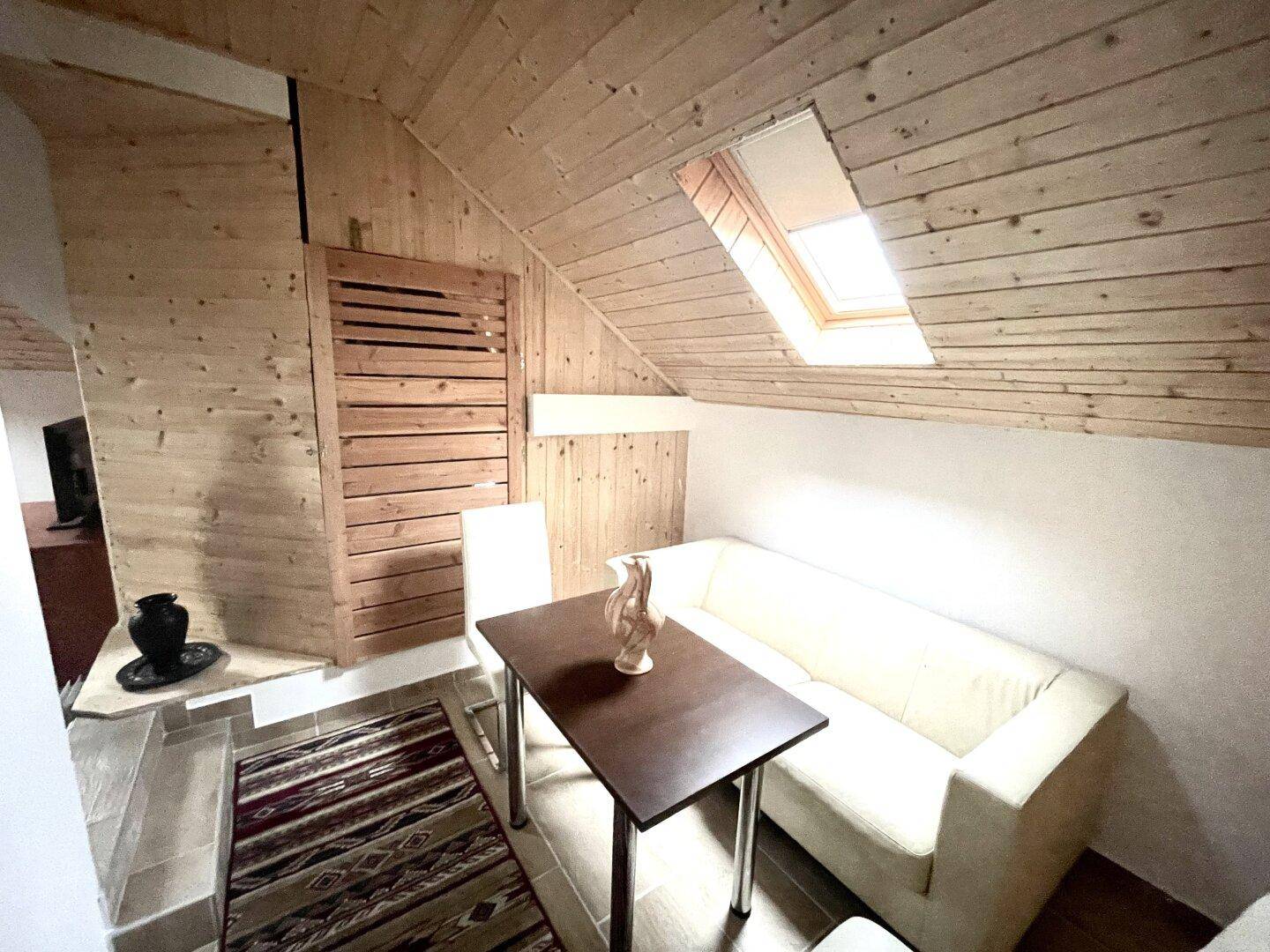 Gemütlicher Wohnbereich im Dachgeschoss mit Holzdachschrägen, Sofa und einem kleinen Tisch.