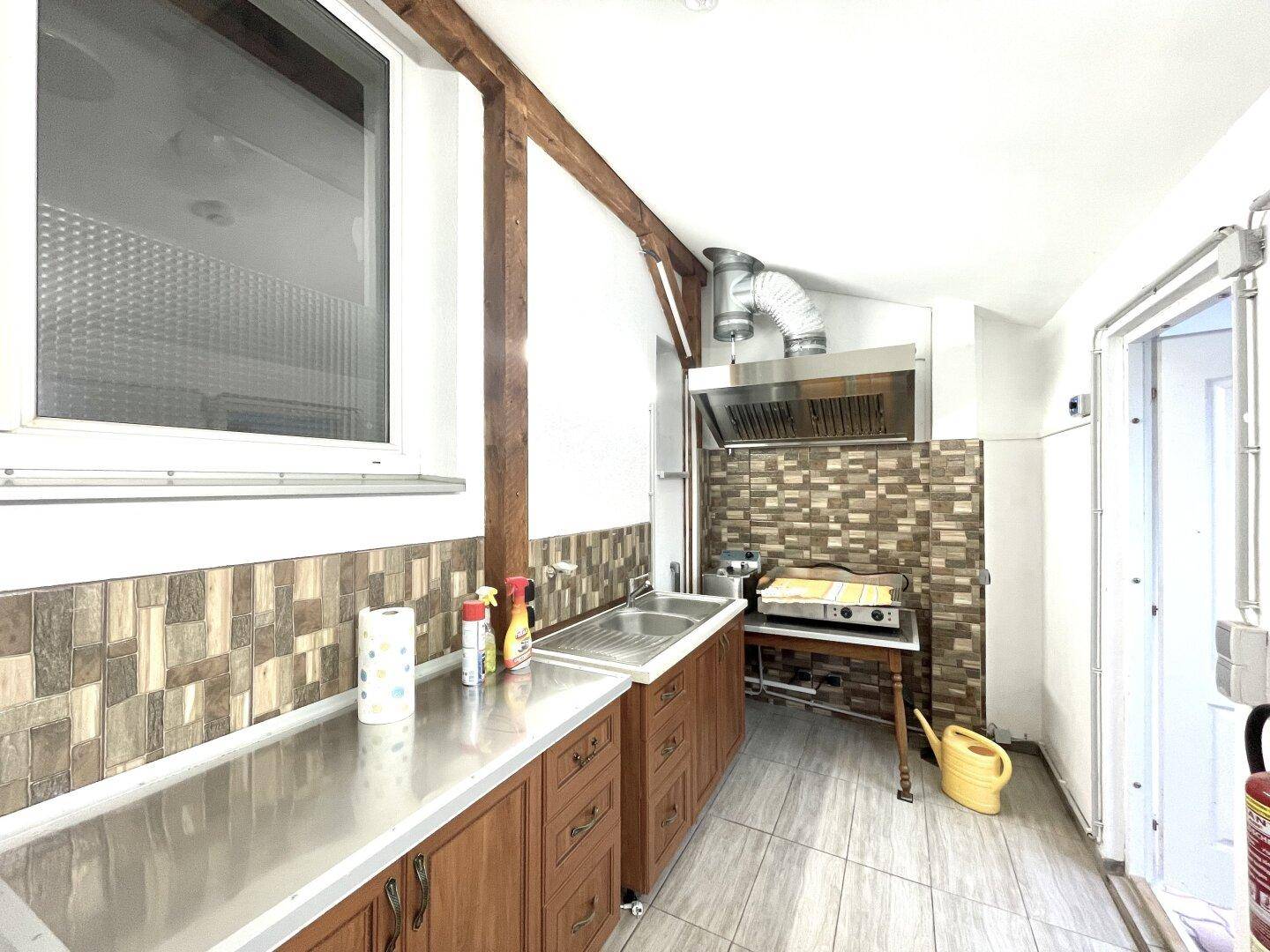 Funktionale Küche mit Holzschränken, Edelstahlspüle und gemusterten Fliesen an der Wand.
