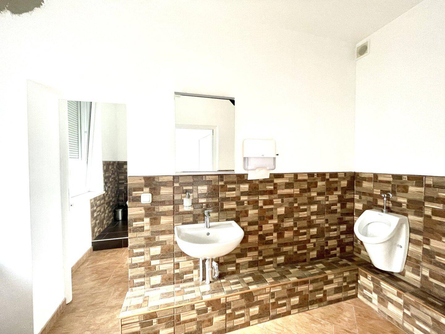 Geräumiges Badezimmer mit Fliesenboden, Urinal und Waschbecken, ideal für gewerbliche Nutzung.