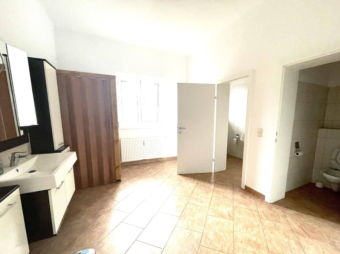 Heller Raum mit Waschtisch und Zugang zu einem separaten WC-Bereich, gefliestem Boden.