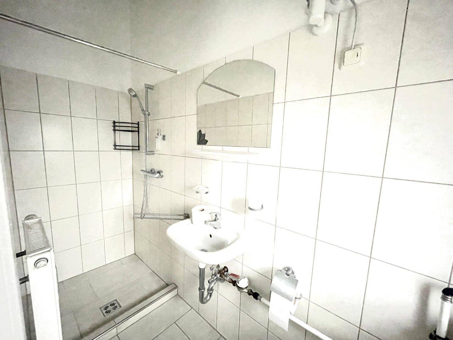 Helles Badezimmer mit ebenerdiger Dusche, Waschbecken und weißen Wandfliesen.