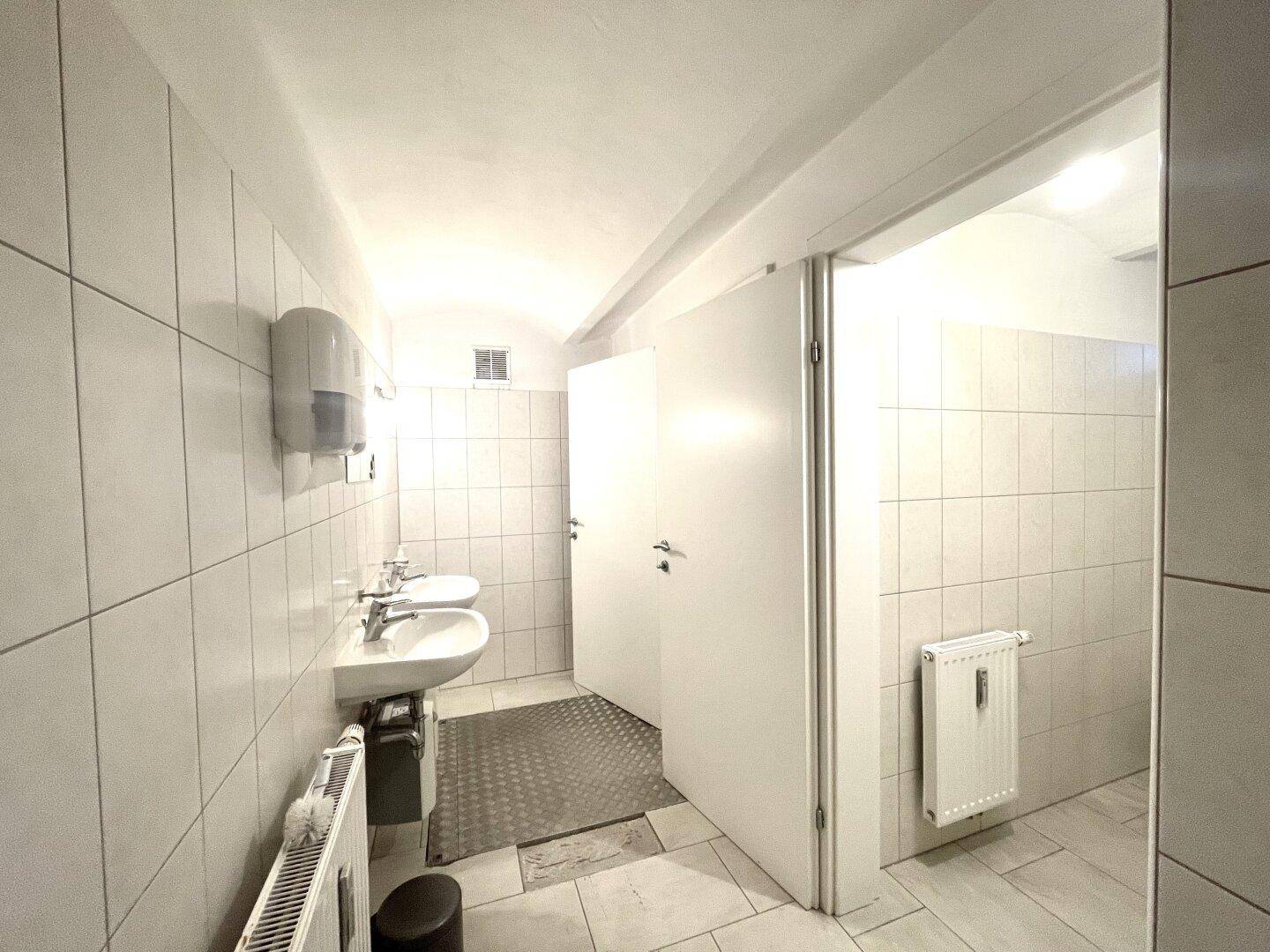 Sanitärbereich mit zwei Waschbecken und weißen Fliesen, gut beleuchtet.