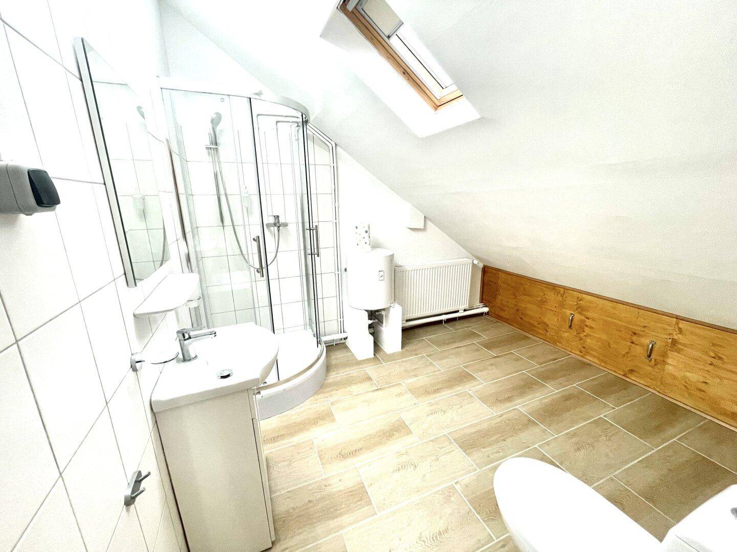 Dachgeschoss-Badezimmer mit Dusche, Waschbecken, WC und Dachfenster, hell und funktional.