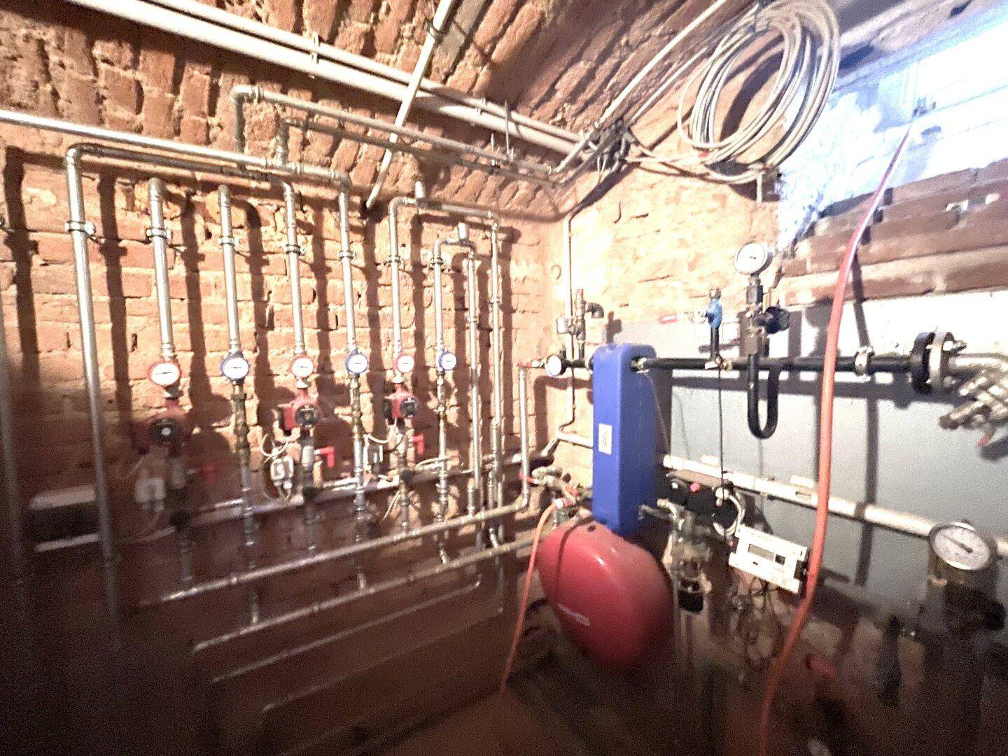 Heizungsraum oder Technikraum mit zahlreichen Rohren und Messgeräten an der Ziegelwand.