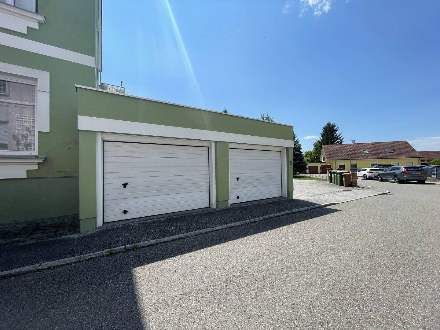 Doppelgarage mit weißen Toren und grün gestrichener Fassade, an einem Wohngebäude.
