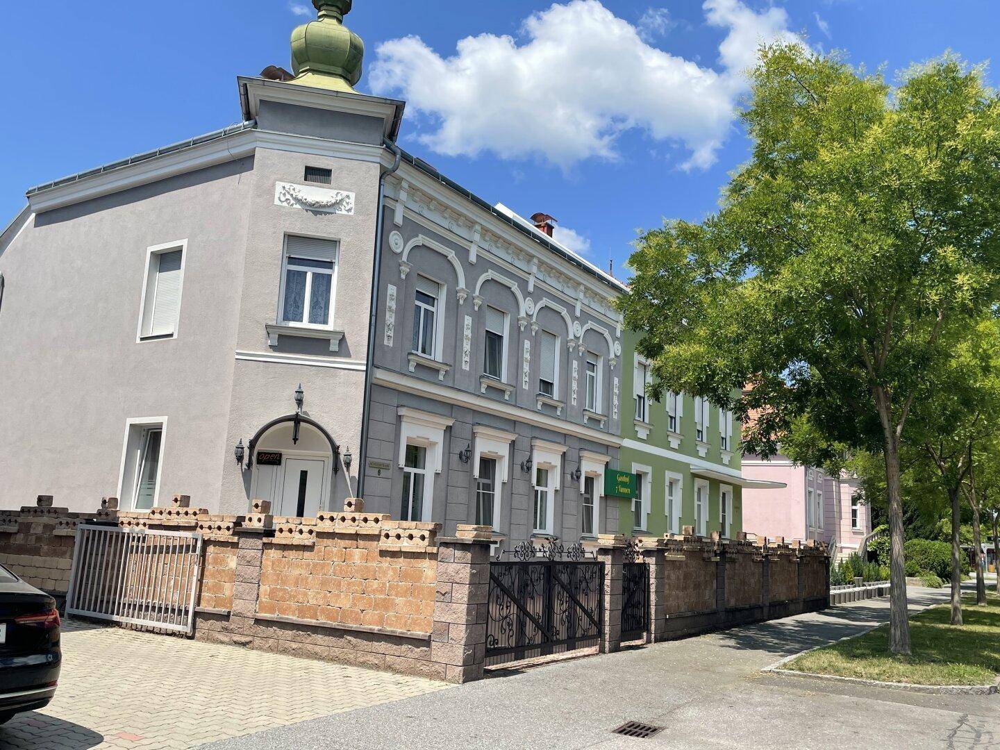 Historisches Gebäude mit dekorativer Fassade und schmiedeeisernem Zaun, an einer Straße gelegen.