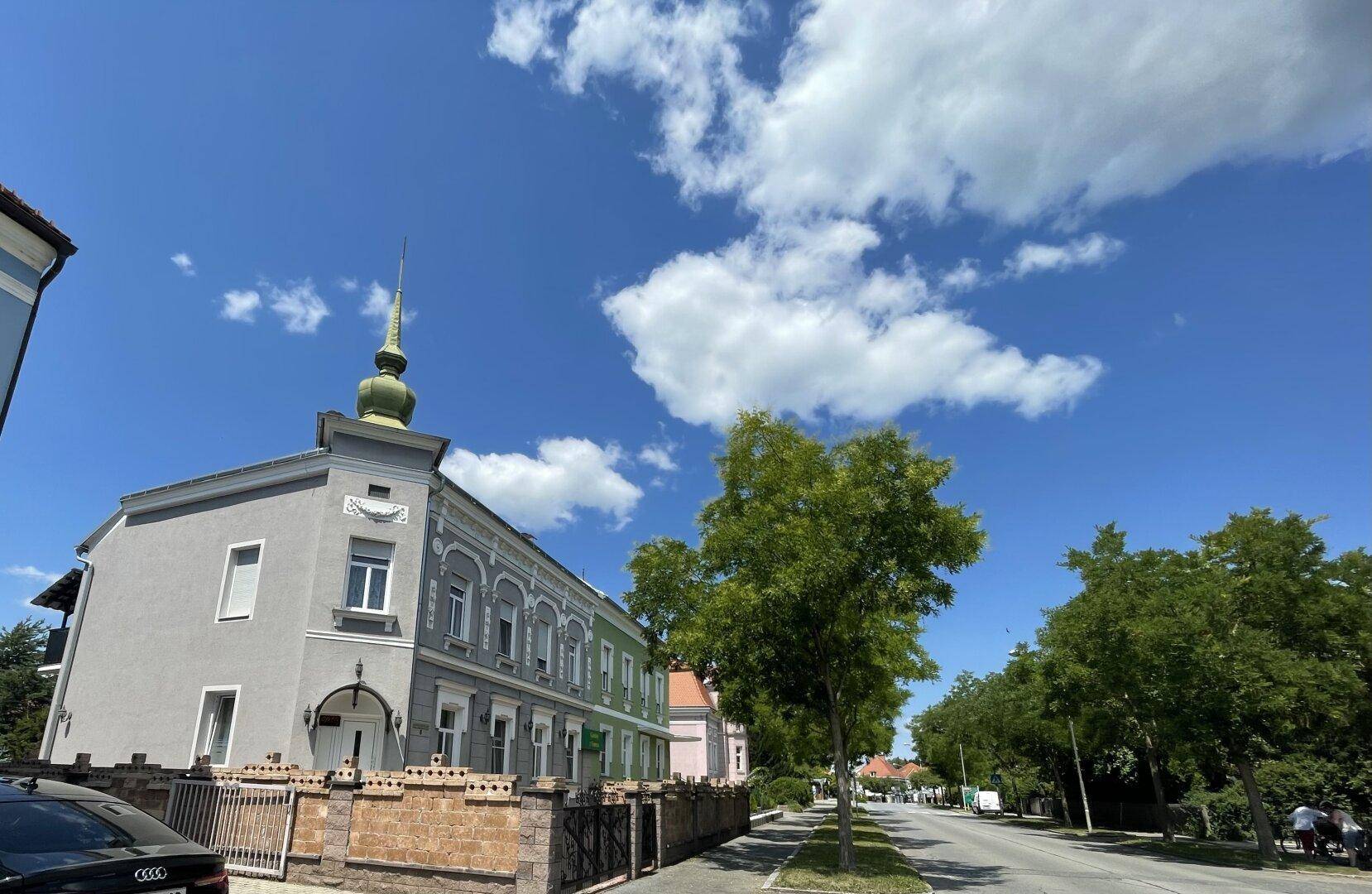 Historisches Gebäude mit markantem Turm und gepflegter Fassade, an einer Allee.