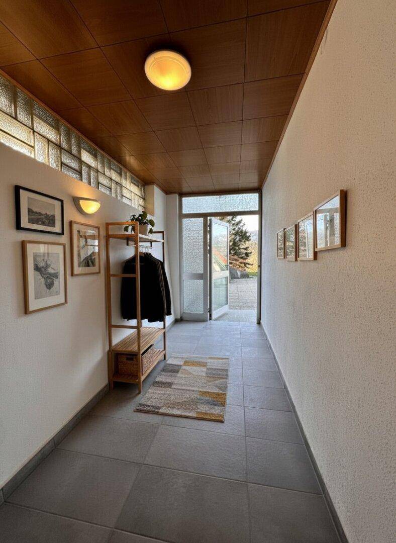 Heller Eingangsbereich mit Fliesenboden, Garderobe und viel Tageslicht durch Glasbausteine.