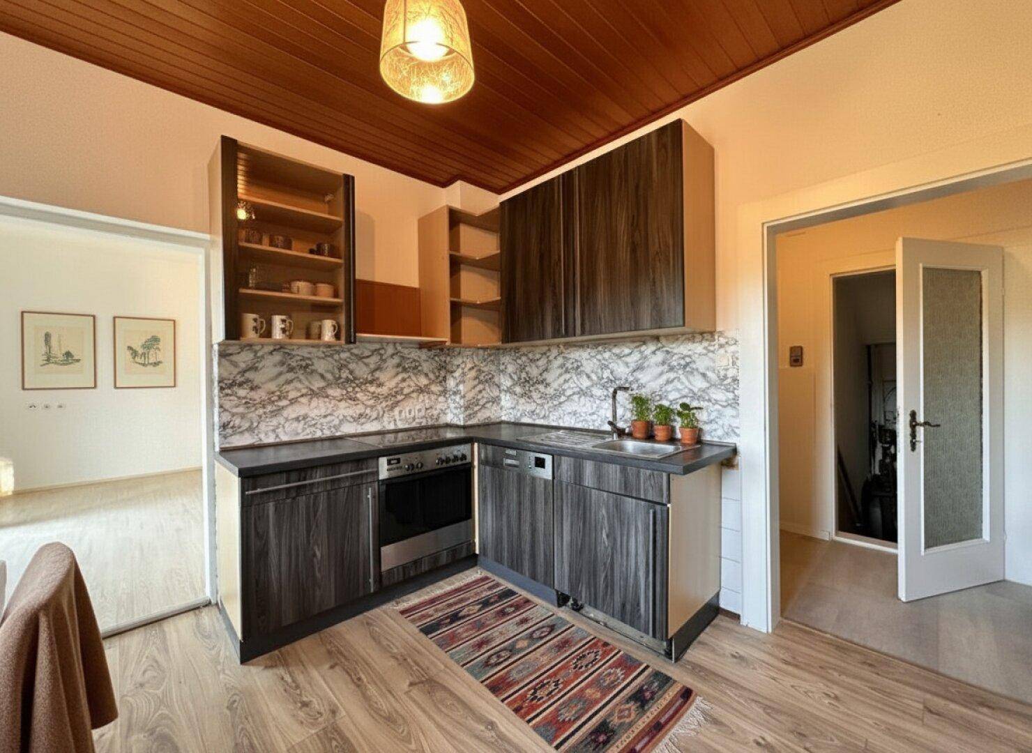 Funktionale Küche mit dunklen Holzfronten, Marmor-Rückwand und integrierten Geräten.