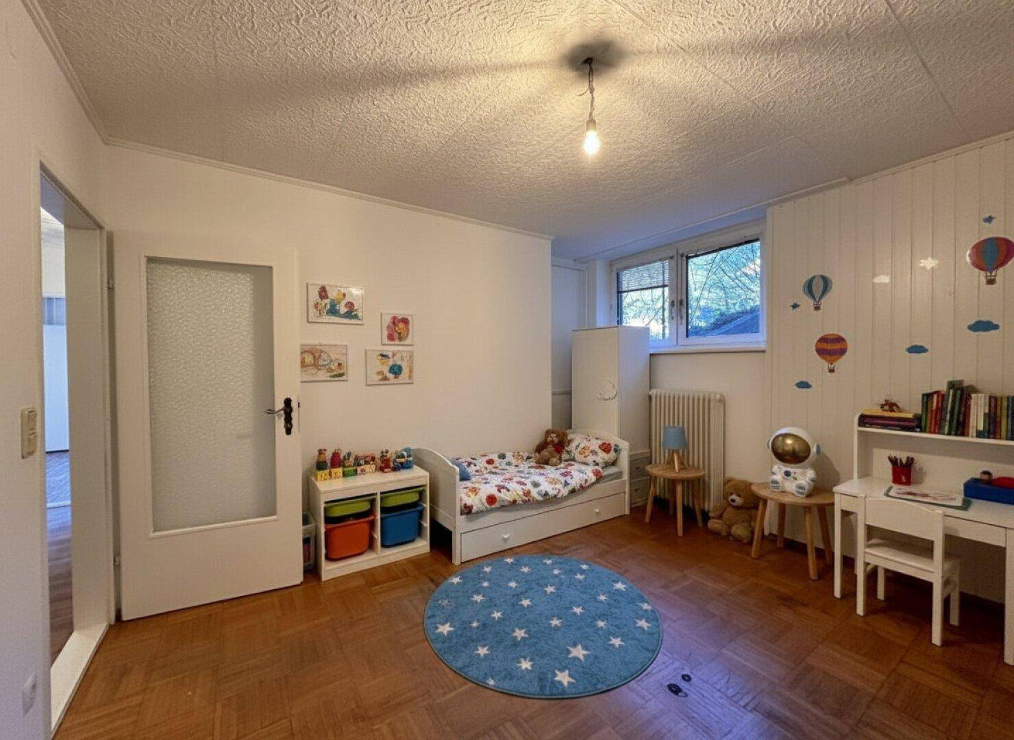 Freundliches Kinderzimmer mit Holzboden, Spielbereich und bunten Wanddekorationen.