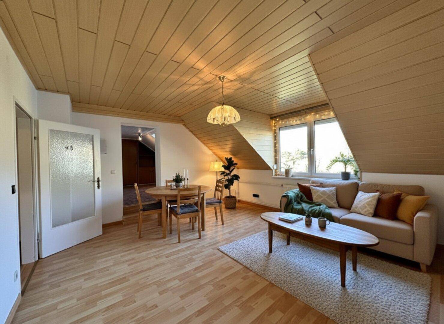 Heller Wohn- und Essbereich im Dachgeschoss mit Holzpaneeldecke und Laminatboden.