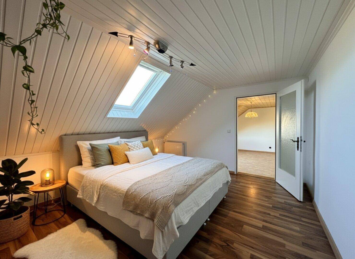 Gemütliches Schlafzimmer im Dachgeschoss mit Holzpaneeldecke, Dachfenster und Holzboden.