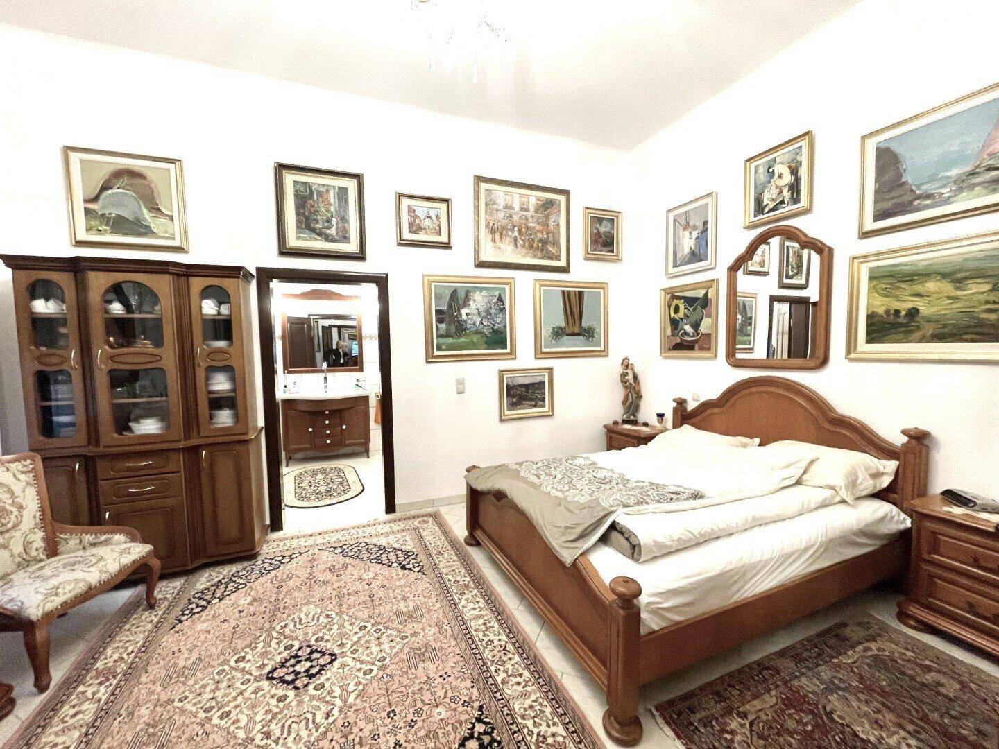 Schlafzimmer mit Holzbett und Nachttischen, Teppichboden und Zugang zu einem angrenzenden Badezimmer.