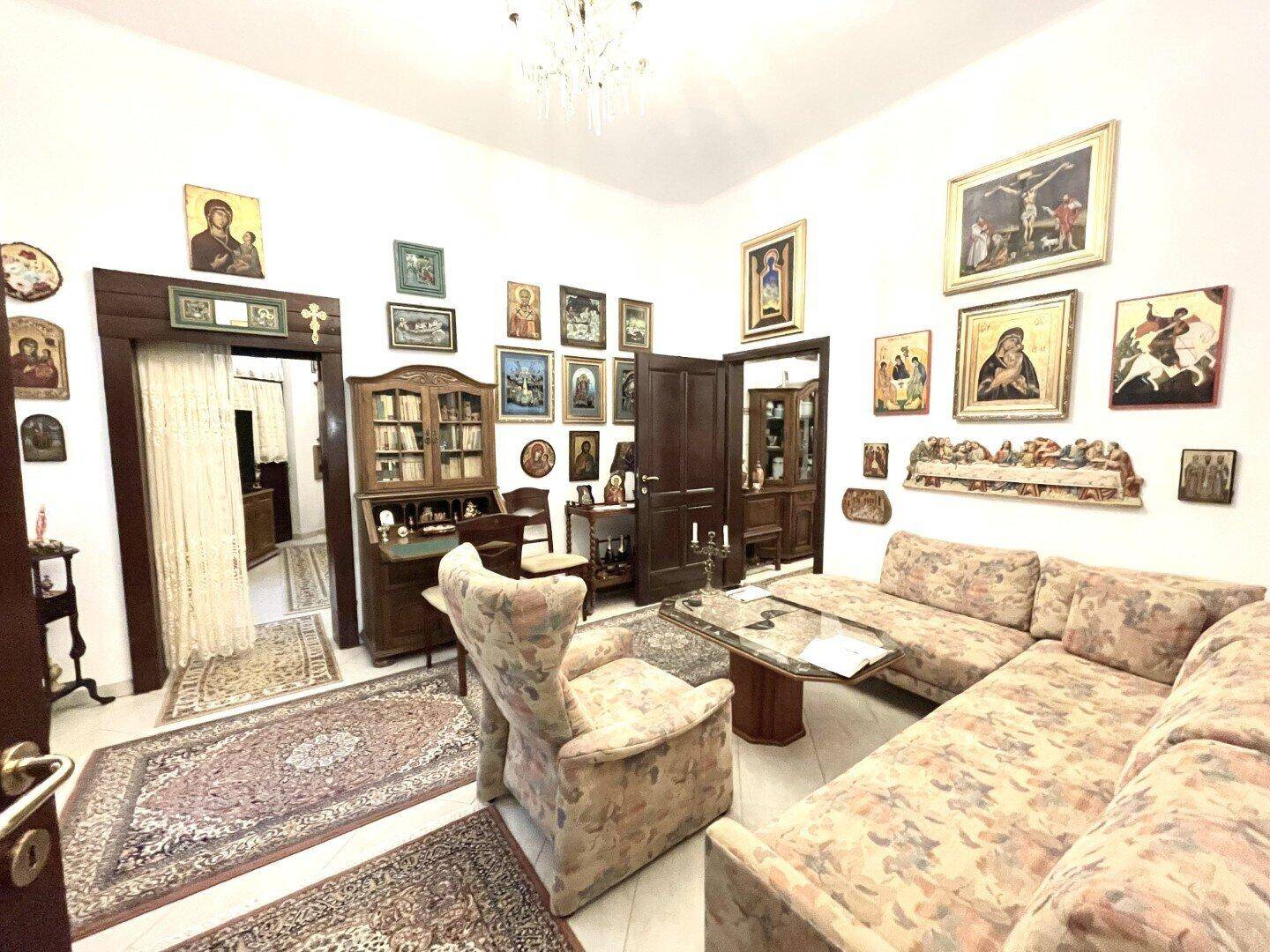 Traditionelles Wohnzimmer mit Ecksofa und antikem Holzschrank, geschmückt mit vielen religiösen Bildern.