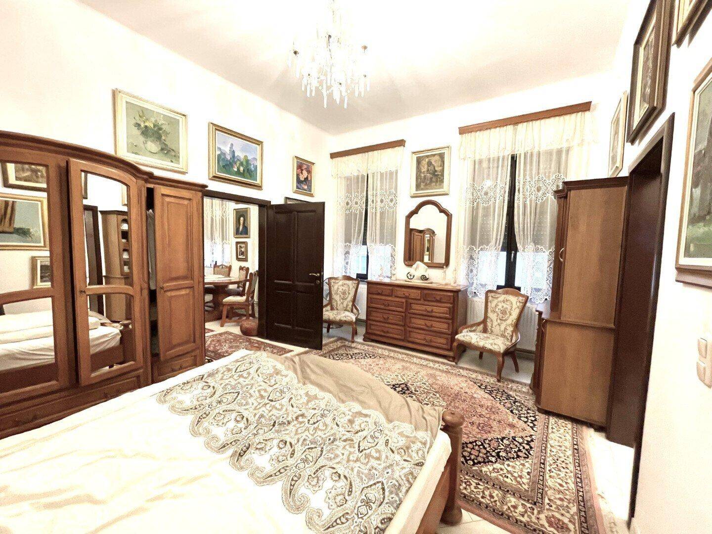 Helles Schlafzimmer mit Holzbett, Kleiderschrank und Fenstern, traditionell eingerichtet mit Teppich.