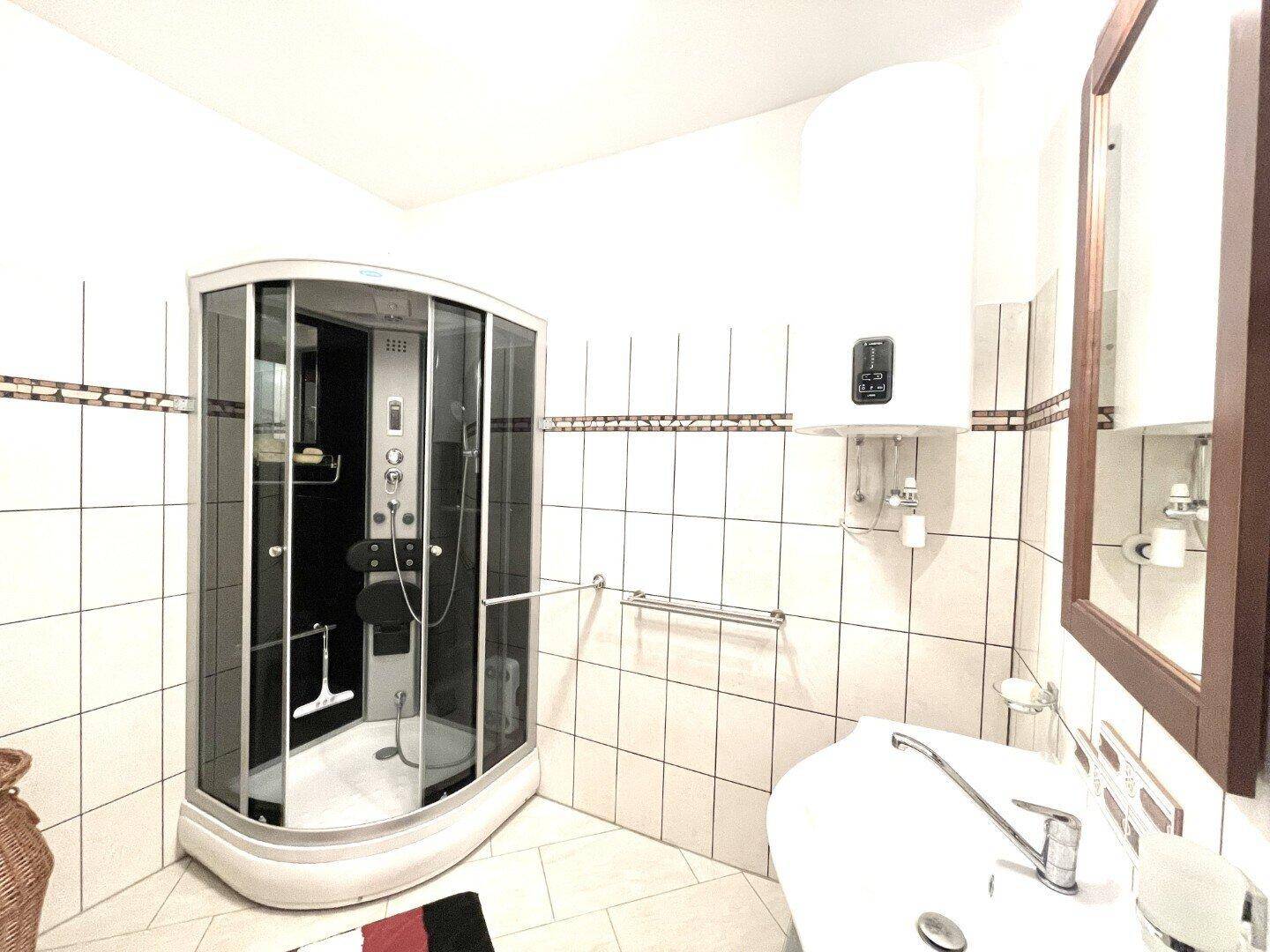 Modernes Badezimmer mit Eckduschkabine und Waschbecken, hell gefliest und funktional eingerichtet.