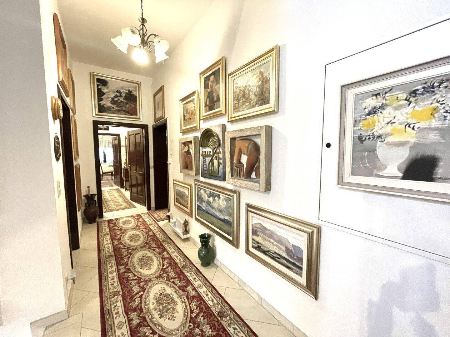 Langer Flur mit Teppichläufer und einer Galerie von gerahmten Bildern an den Wänden.