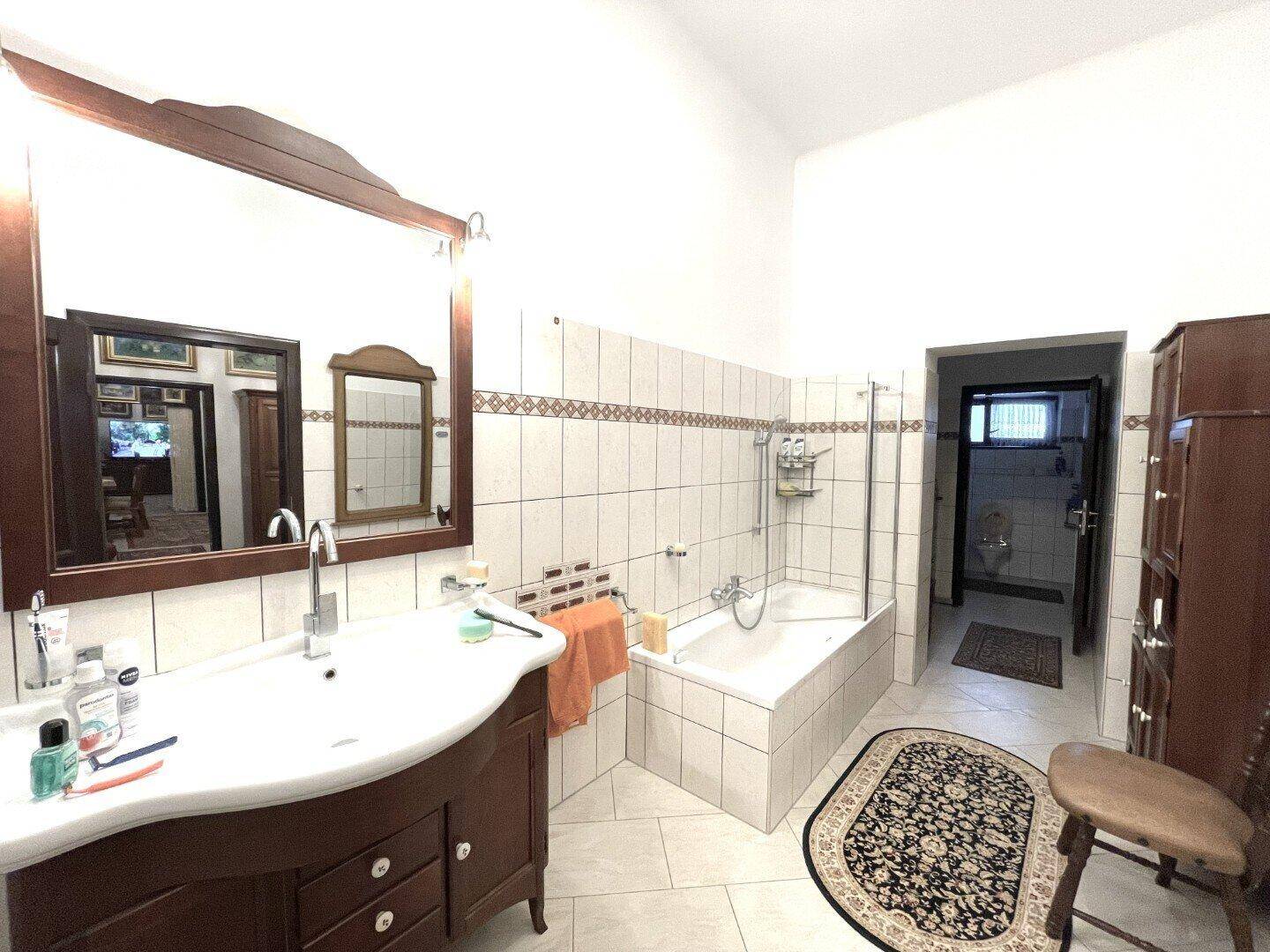 Geräumiges Badezimmer mit Waschtisch, Spiegel und Badewanne mit Duschfunktion, komplett gefliest.