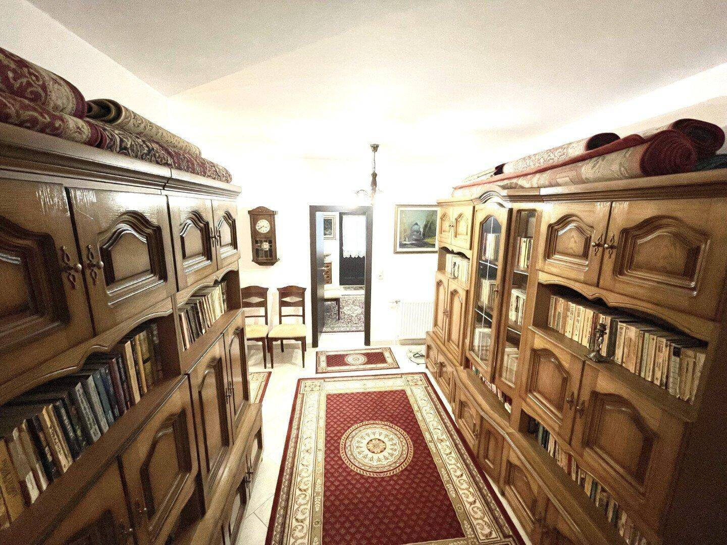 Langer Flur oder Bibliothek mit hohen Holzregalen voller Bücher und traditionellen Teppichen.