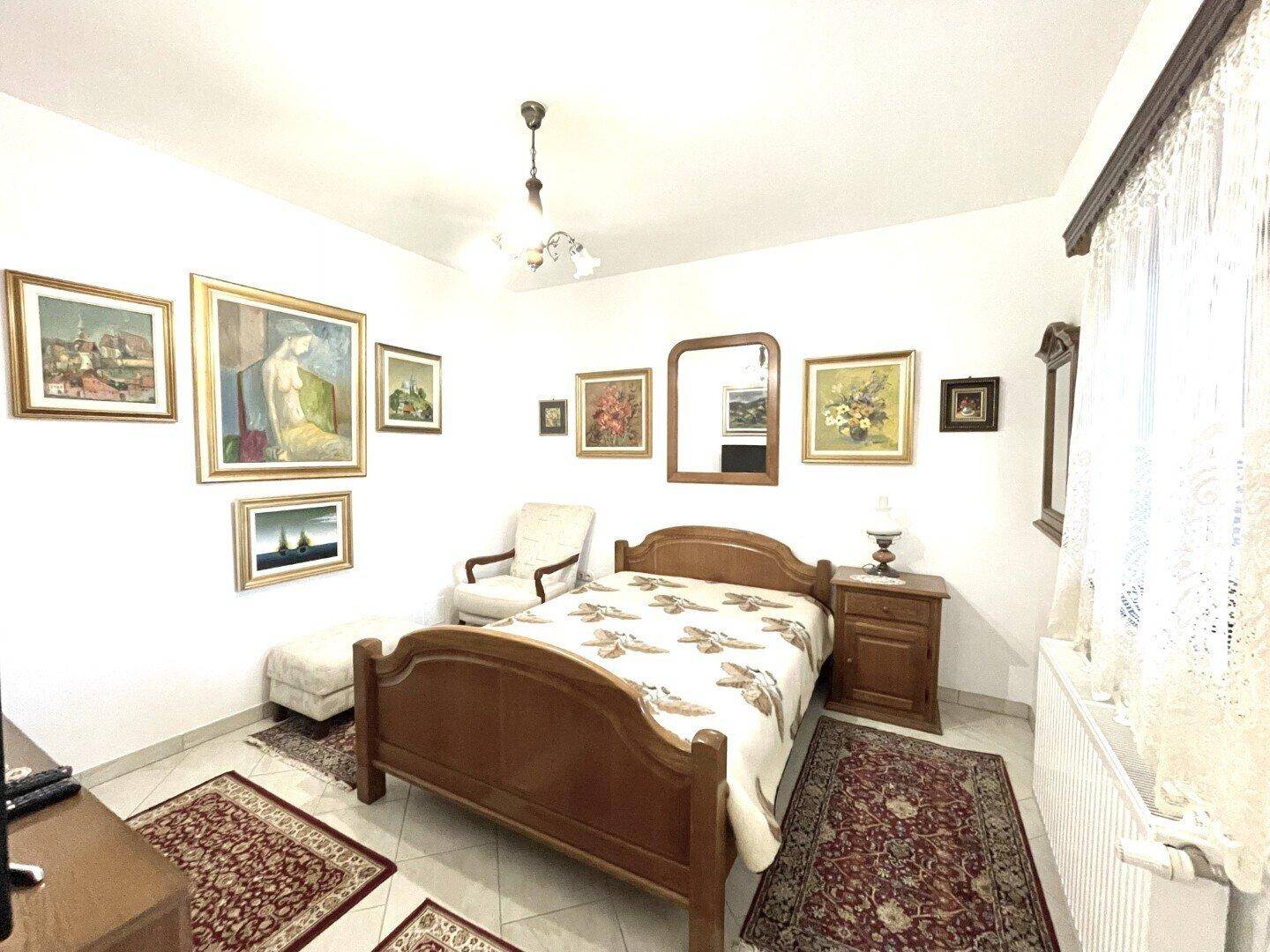 Gemütliches Schlafzimmer mit Holzbett, Nachttisch und großem Teppich, hell und traditionell eingerichtet.