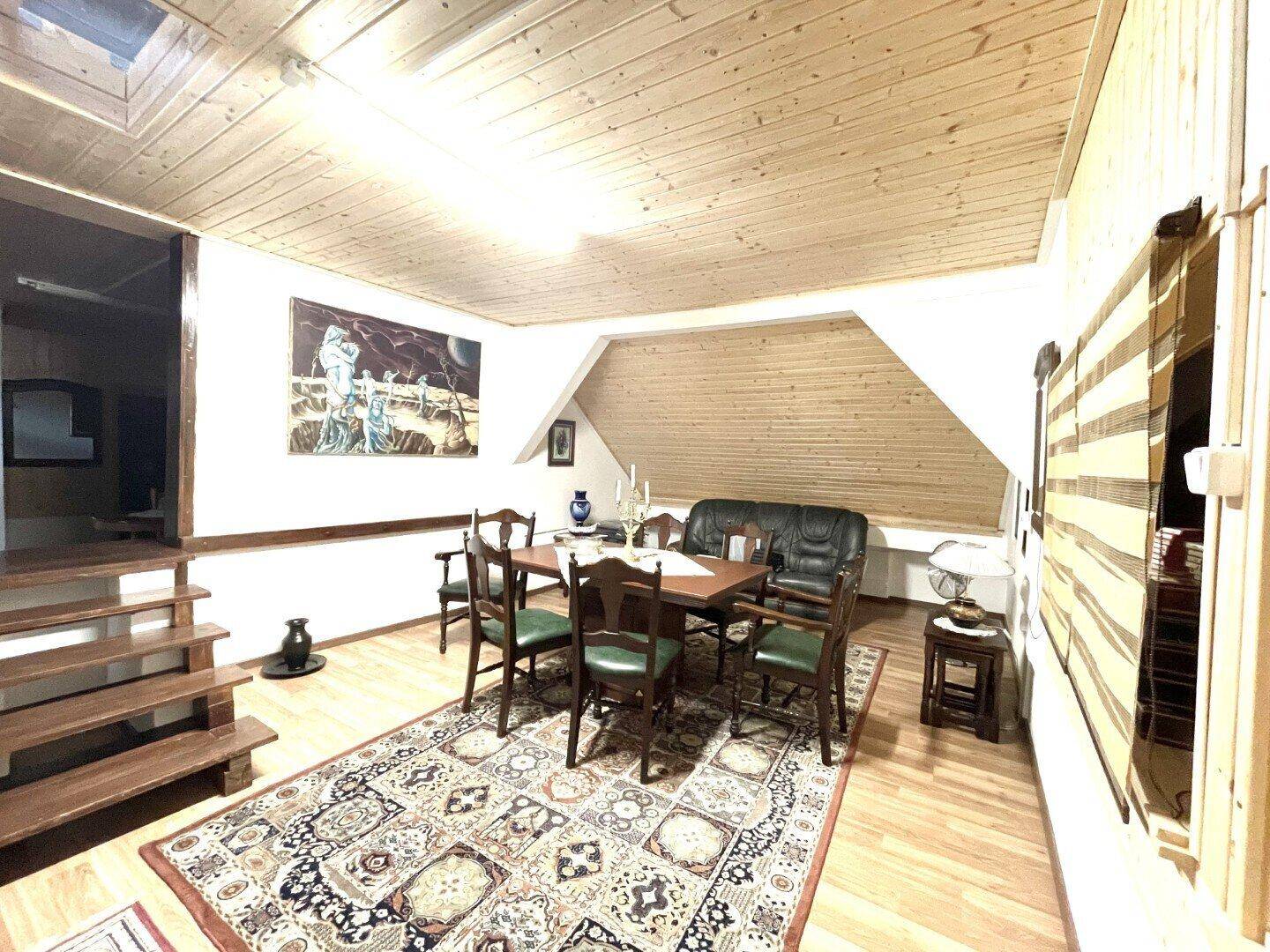 Gemütlicher Dachbodenraum mit Holzverkleidung, Esstisch und Sofa, ideal für Wohn- und Essbereich.