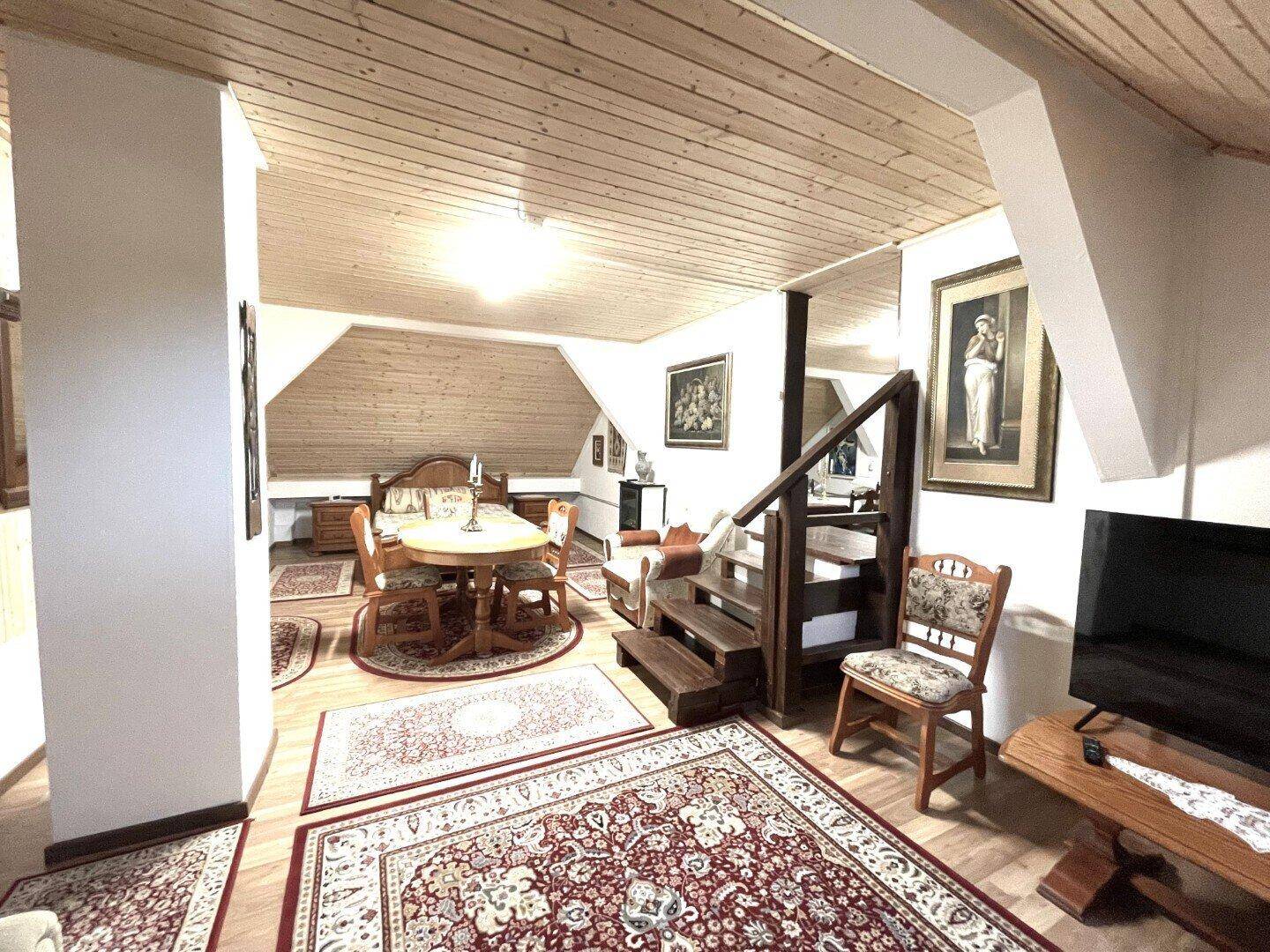 Vielseitiger Dachbodenraum mit Holzdecken, Essbereich und Schlafgelegenheit, hell und geräumig.