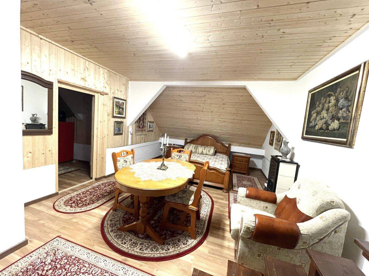 Heller Dachbodenraum mit Holzverkleidung, Esstisch und Bett, kombiniert Wohn- und Schlafbereich.