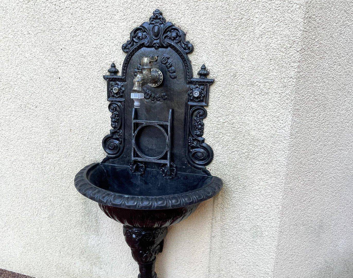 Dekorativer Wandbrunnen aus Gusseisen, ein charmantes Detail an der Außenfassade des Gebäudes.