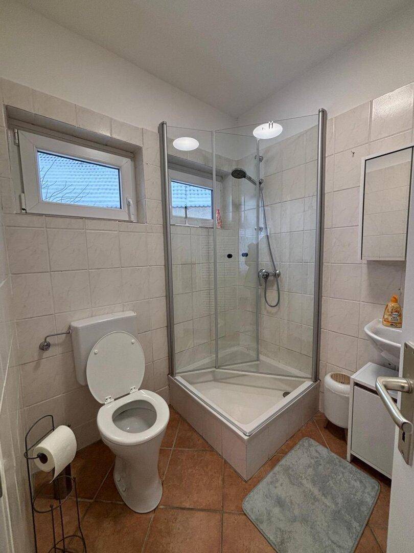 Badezimmer mit Eckduschkabine, Toilette und Fenster für Belüftung.