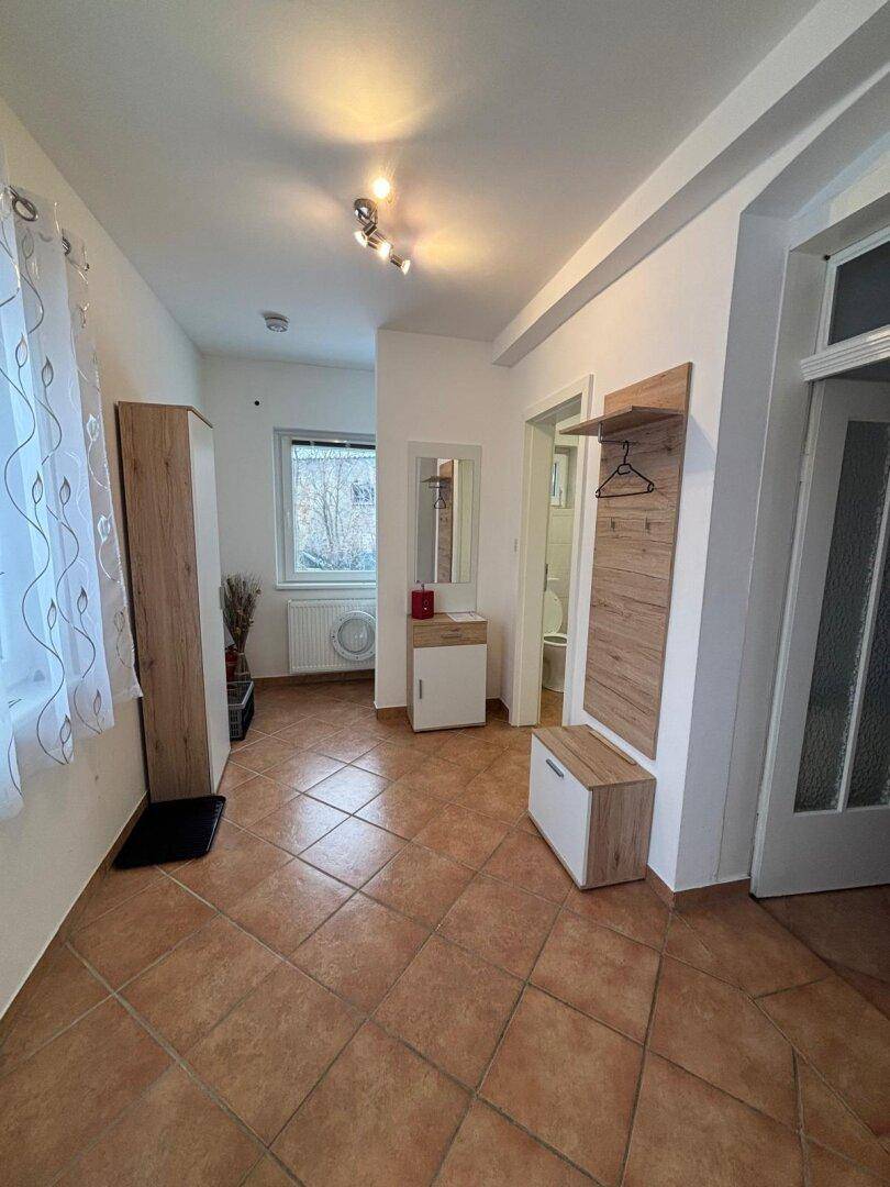 Eingangsbereich mit Terrakottafliesen, Garderobe und einem Fenster.