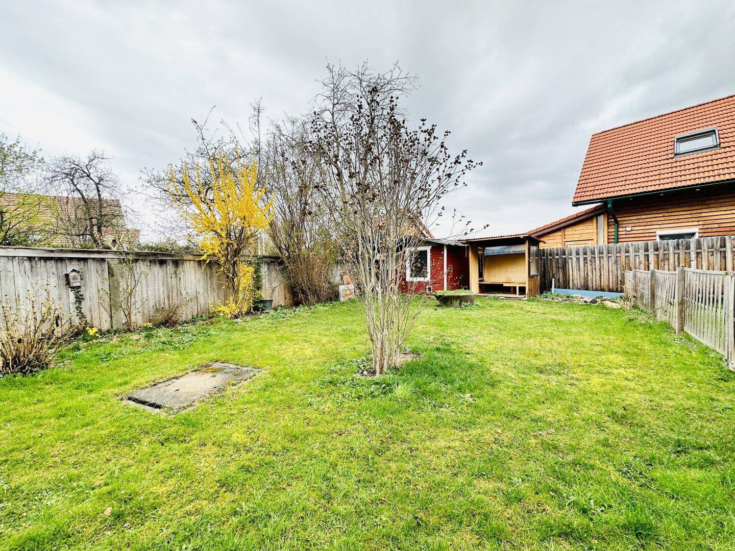Großer Gartenbereich mit Rasen, Bäumen und einem kleinen Schuppen im Hintergrund.