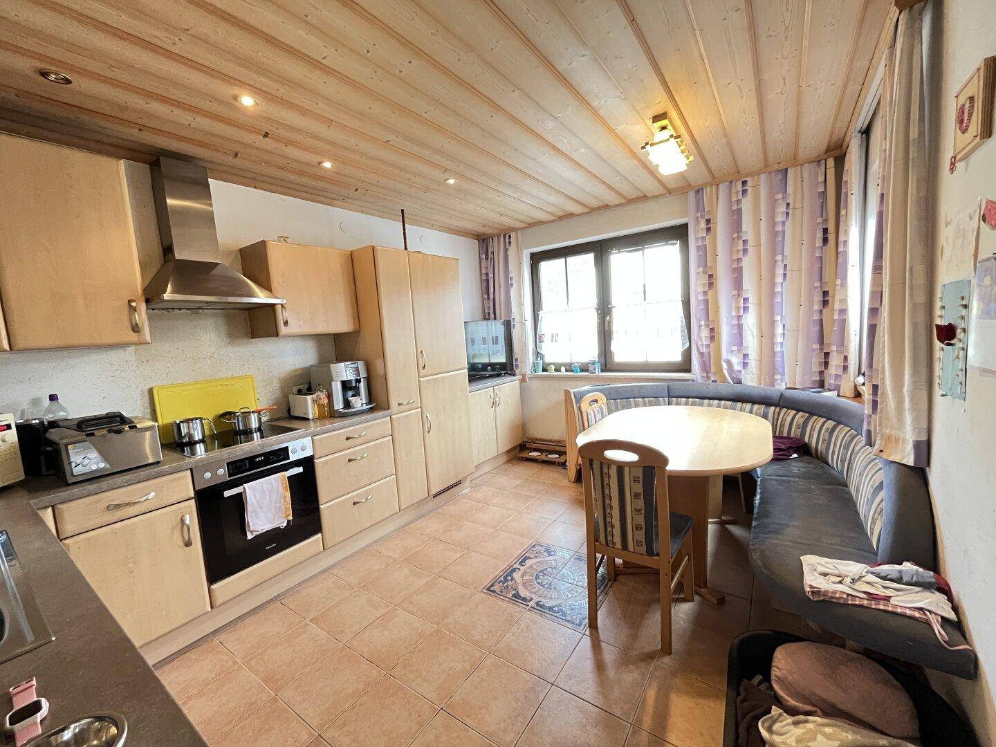 Gemütliche Wohnküche im Landhausstil mit Holzbalkendecke und Essecke.