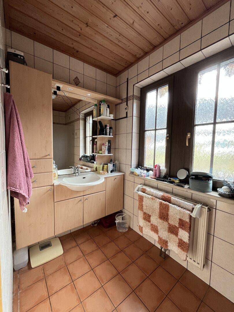 Badezimmer mit Holzdecke, Fliesenboden, Einzelwaschbecken und Fenster.