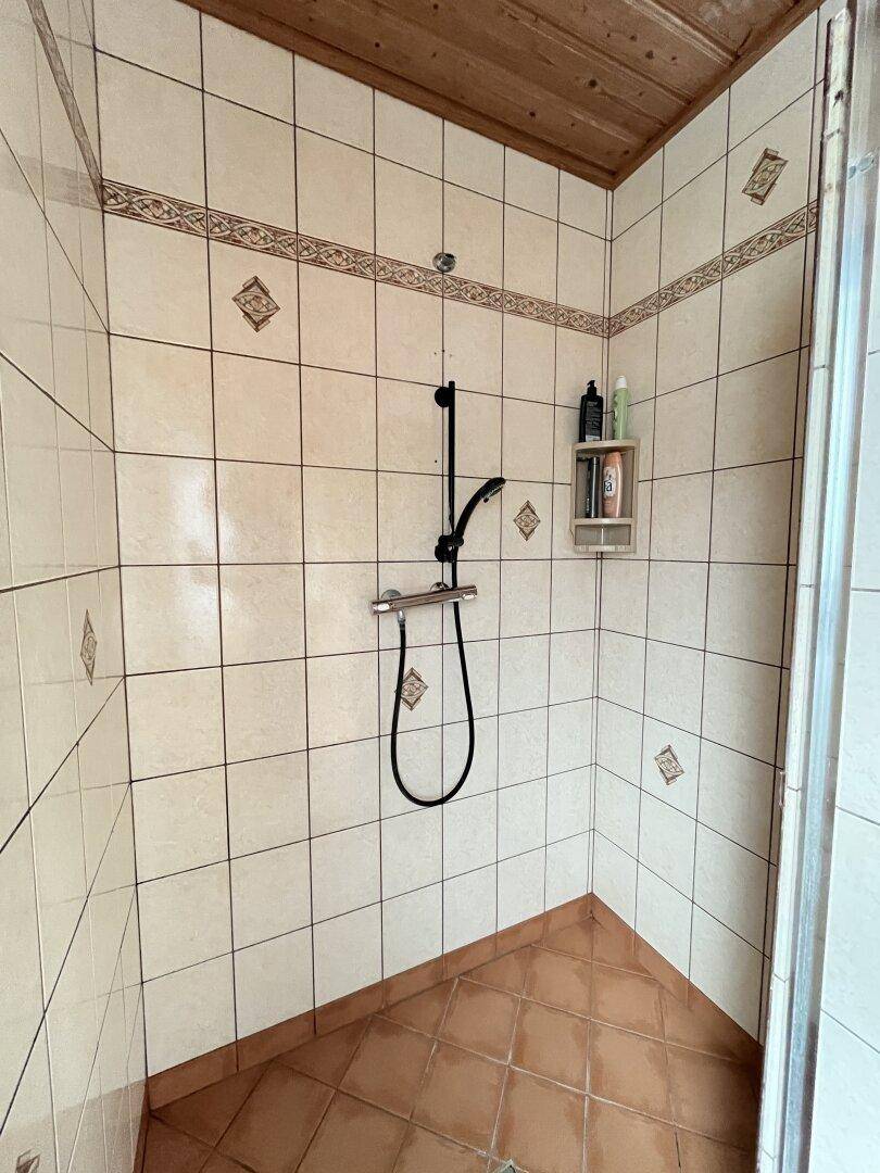 Geflieste Dusche mit Duschkopf und einfacher Ausstattung im Badezimmer.