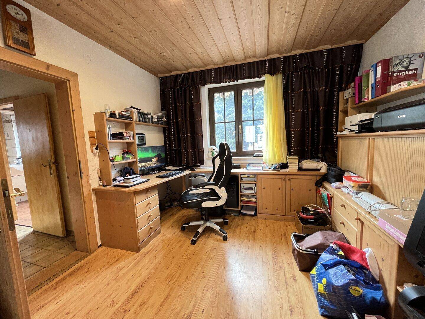 Arbeitszimmer mit Holzdecke, Laminatboden und großem Schreibtisch am Fenster.
