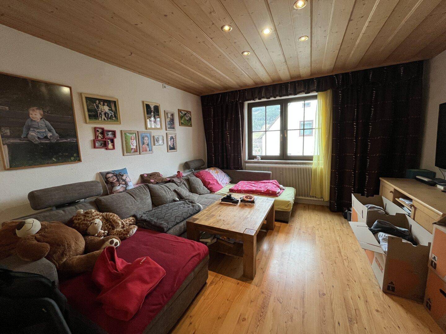 Wohnzimmer mit großem Sofa, Holzbalkendecke und Laminatboden.