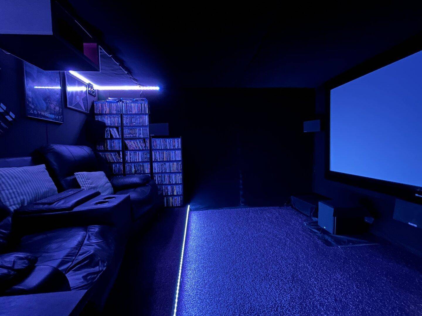 Heimkino mit großer Leinwand, bequemen Sitzen und blauer LED-Beleuchtung.
